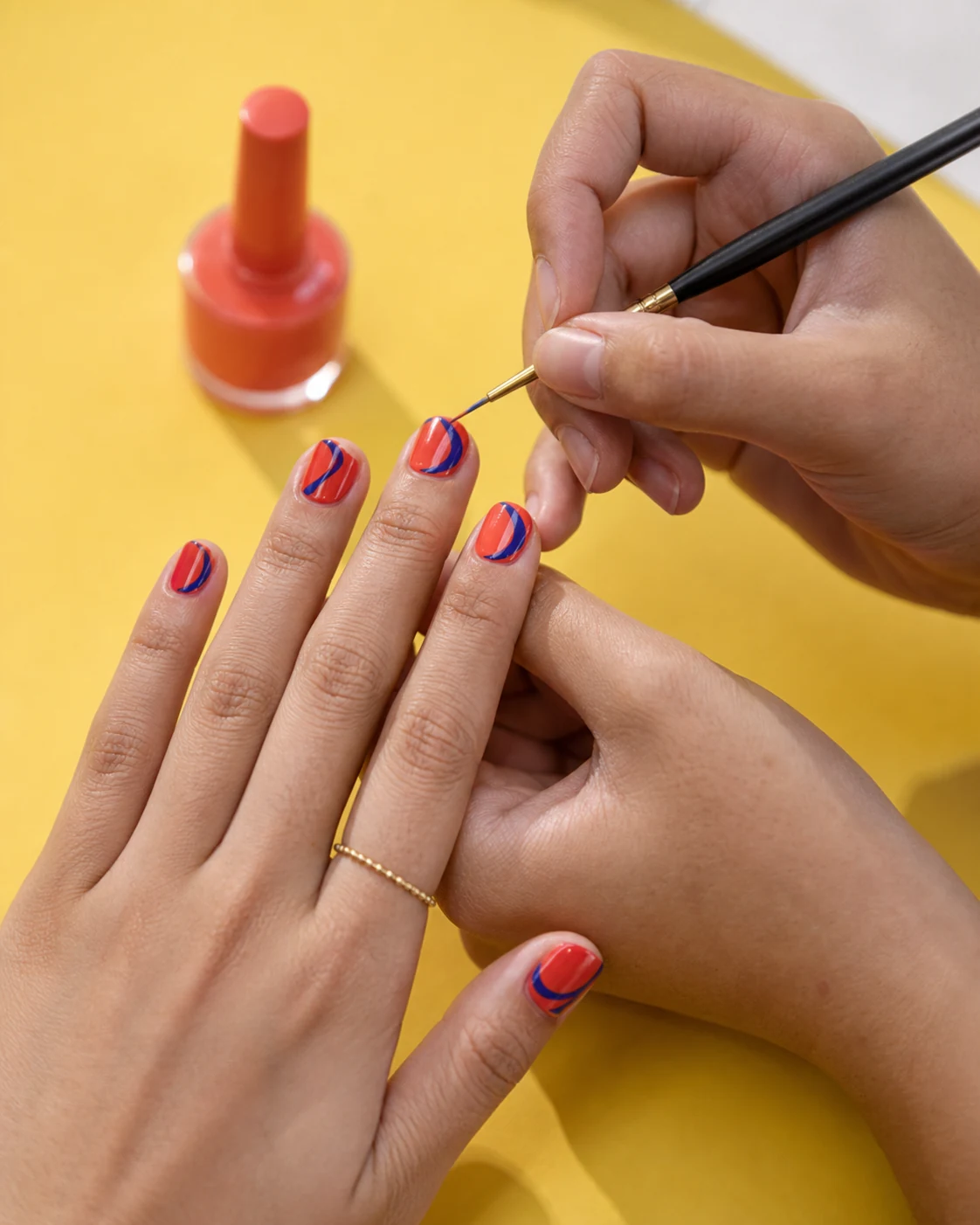 Nail artist hand-painting a cobalt detail on a coral manicure